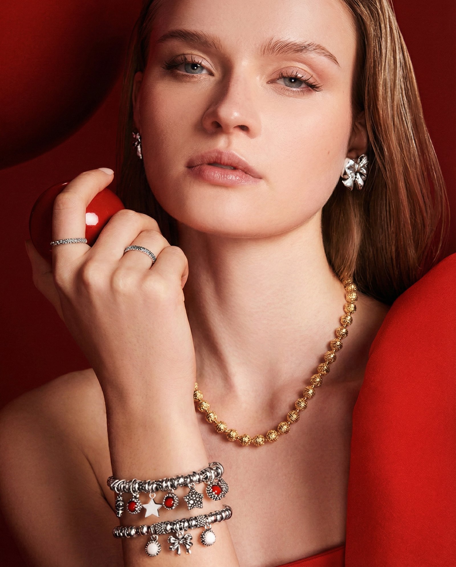 Model in red with layered charm bracelets and a gold necklace