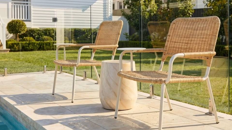 Aris stone side table between two chairs beside a pool